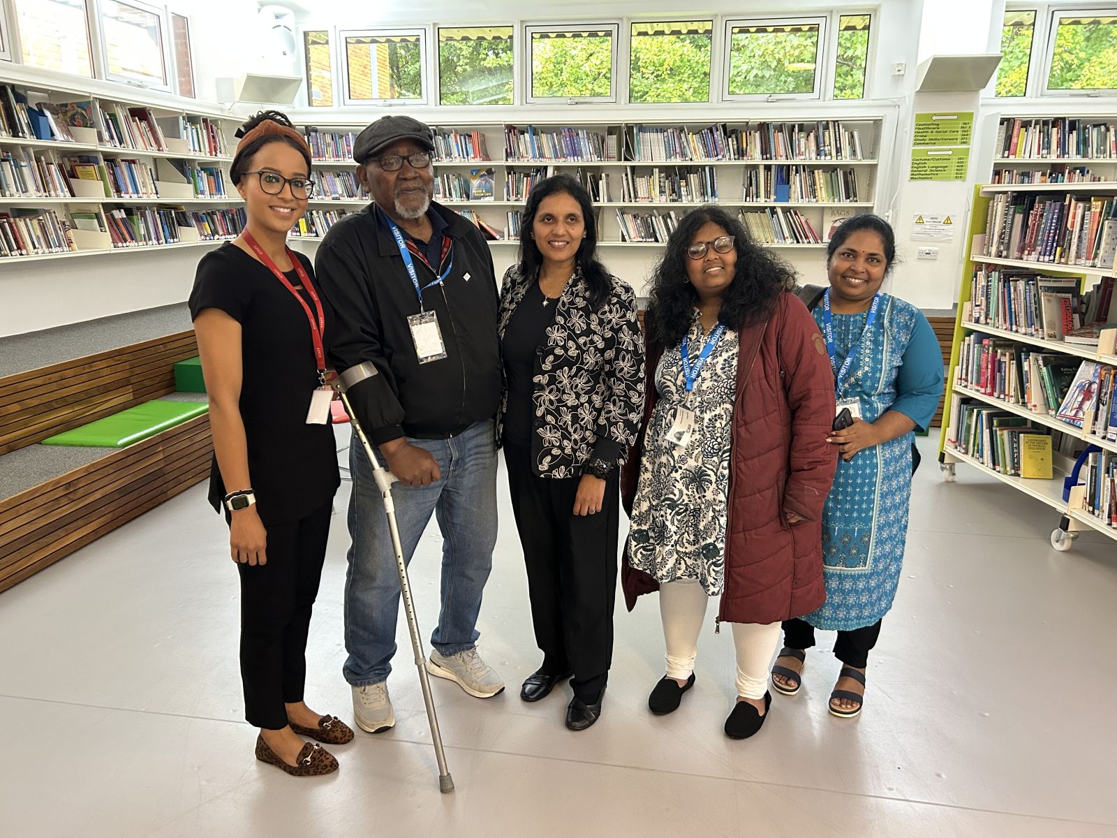 Four women and a man stood in front of a wall of books all smiling 