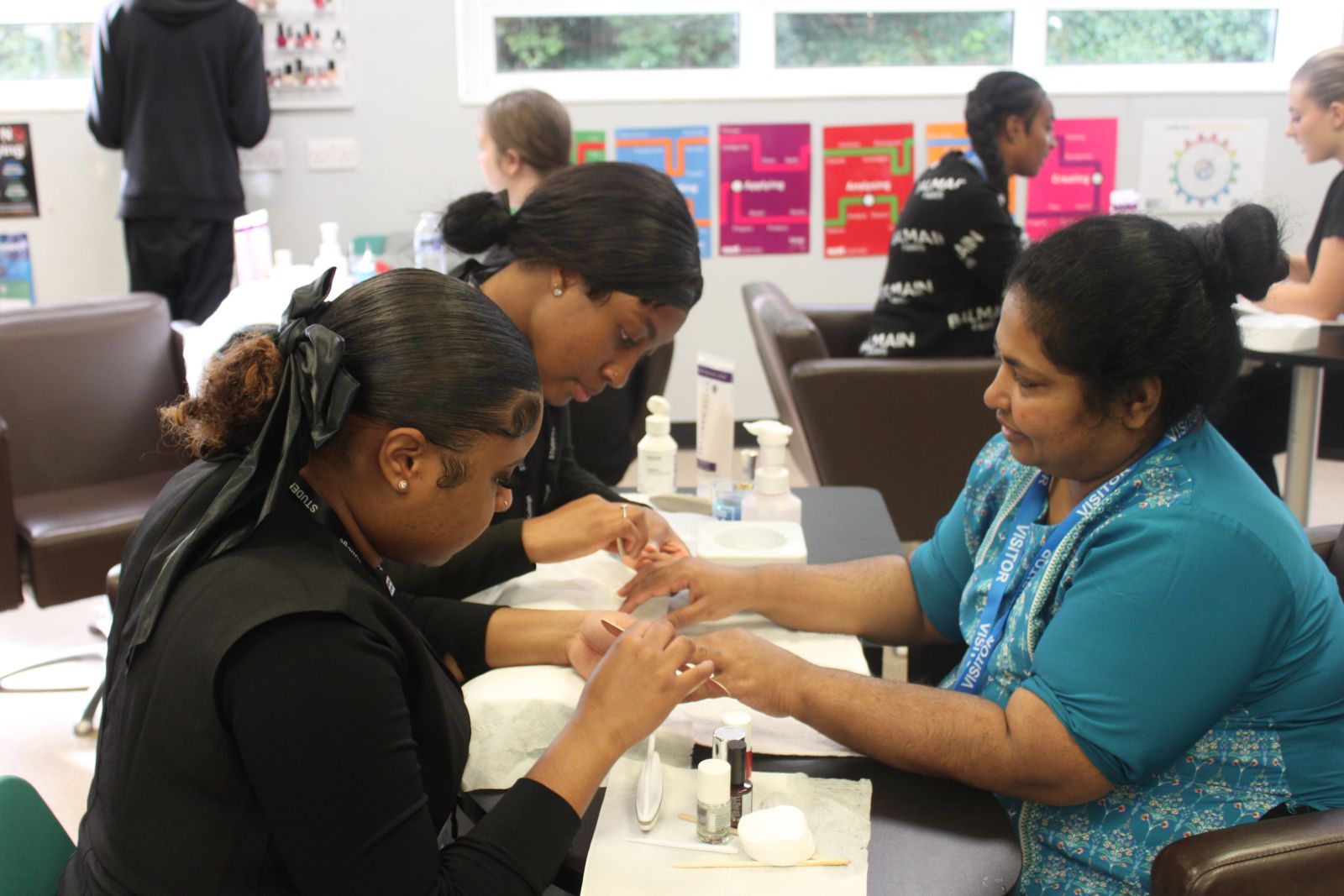 Two students working on a womans hand as they give her a manicure