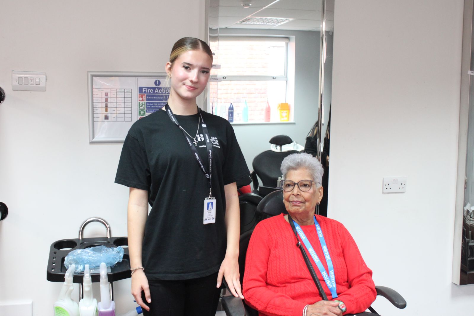 A younger student stood beside an elderly woman sat in the hairdressing chair, both smiling